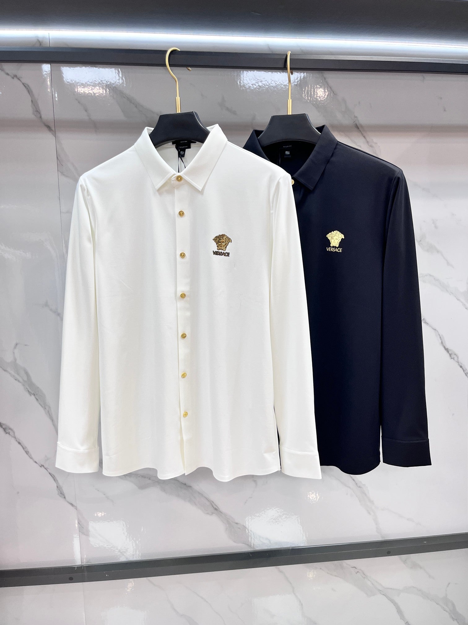 Pair of long-sleeve button-up shirts: white and navy, each with gold logo crest