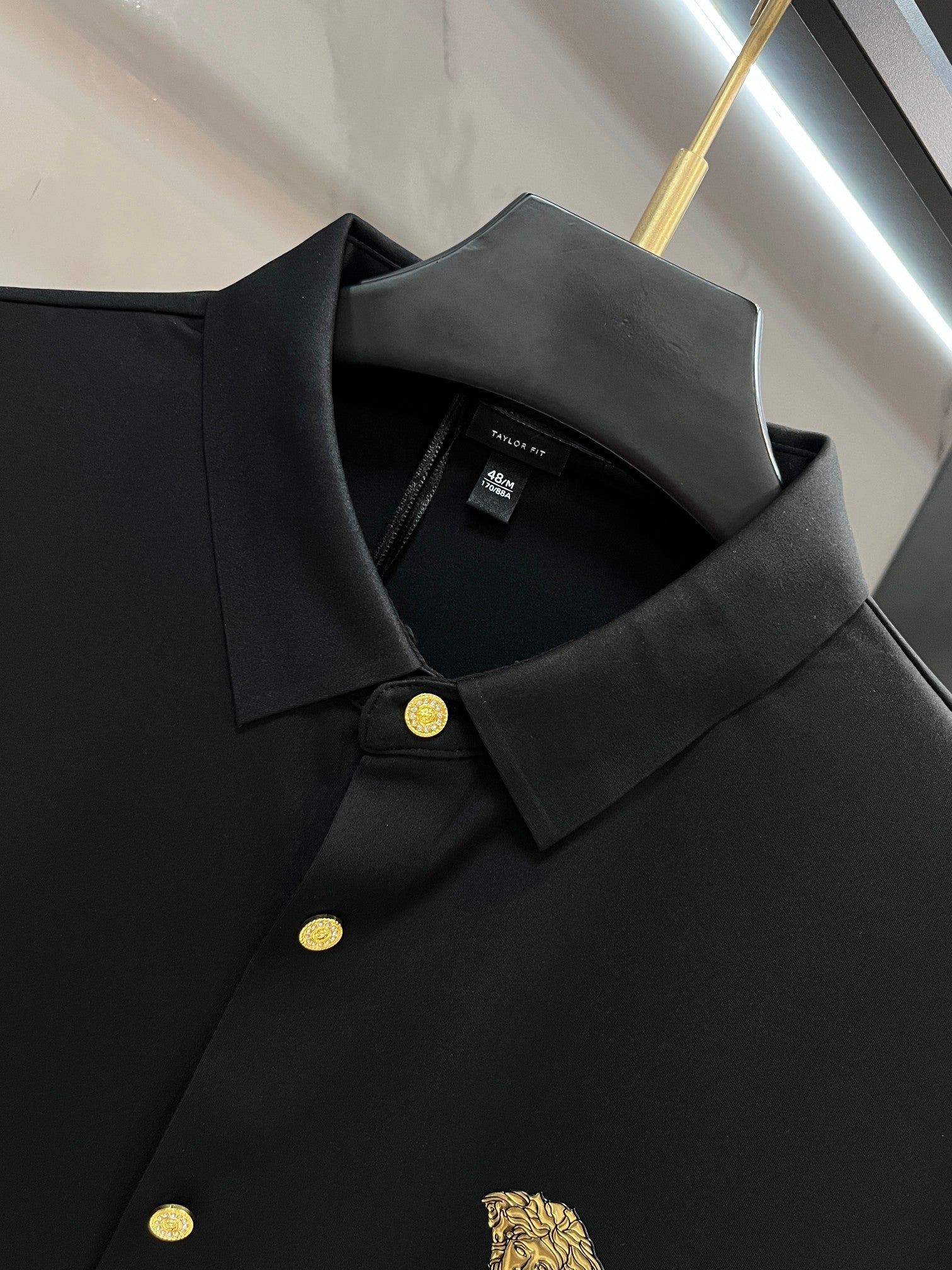 Black long-sleeve button-up shirt close-up, point collar and gold logo button
