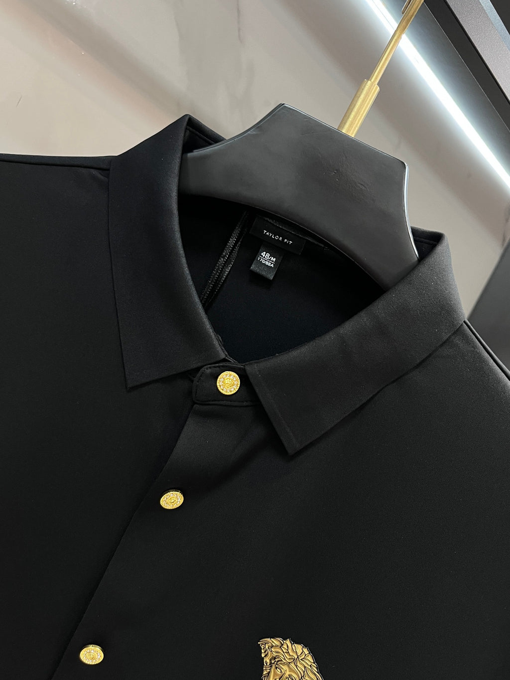 Black long-sleeve polo-style shirt with collar and gold button placket, chest crest