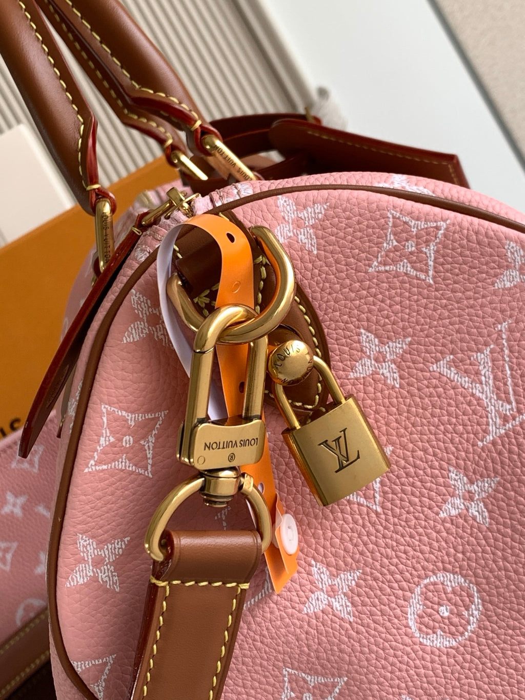Louis Vuitton pink monogram bag with brass hardware, charm accents, and tan leather strap