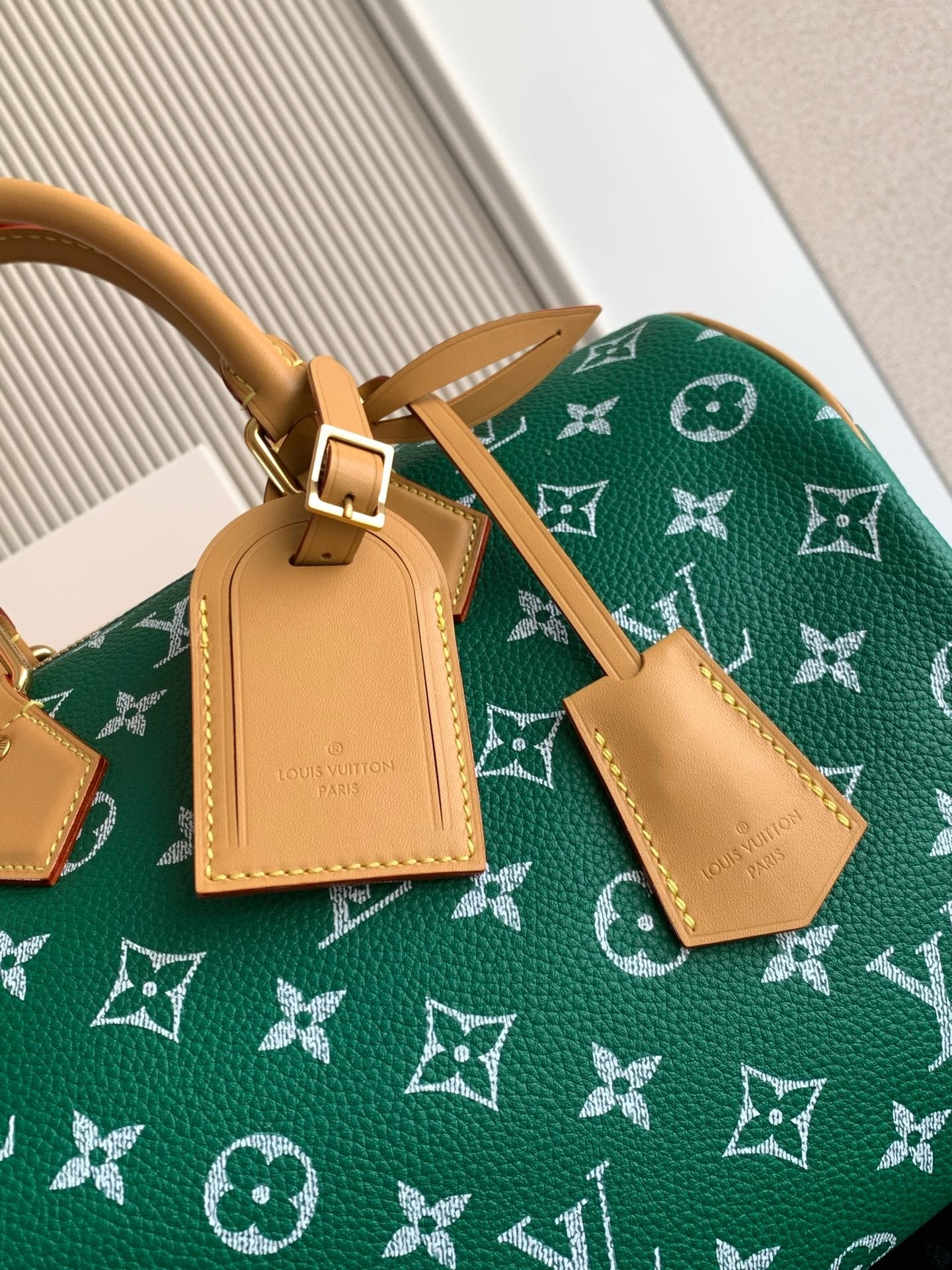 Louis Vuitton green monogram bag closeup with tan leather trim and hanging charm
