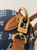 Designer handbag close-up of tan leather tab and gold ring clasp on navy monogram canvas
