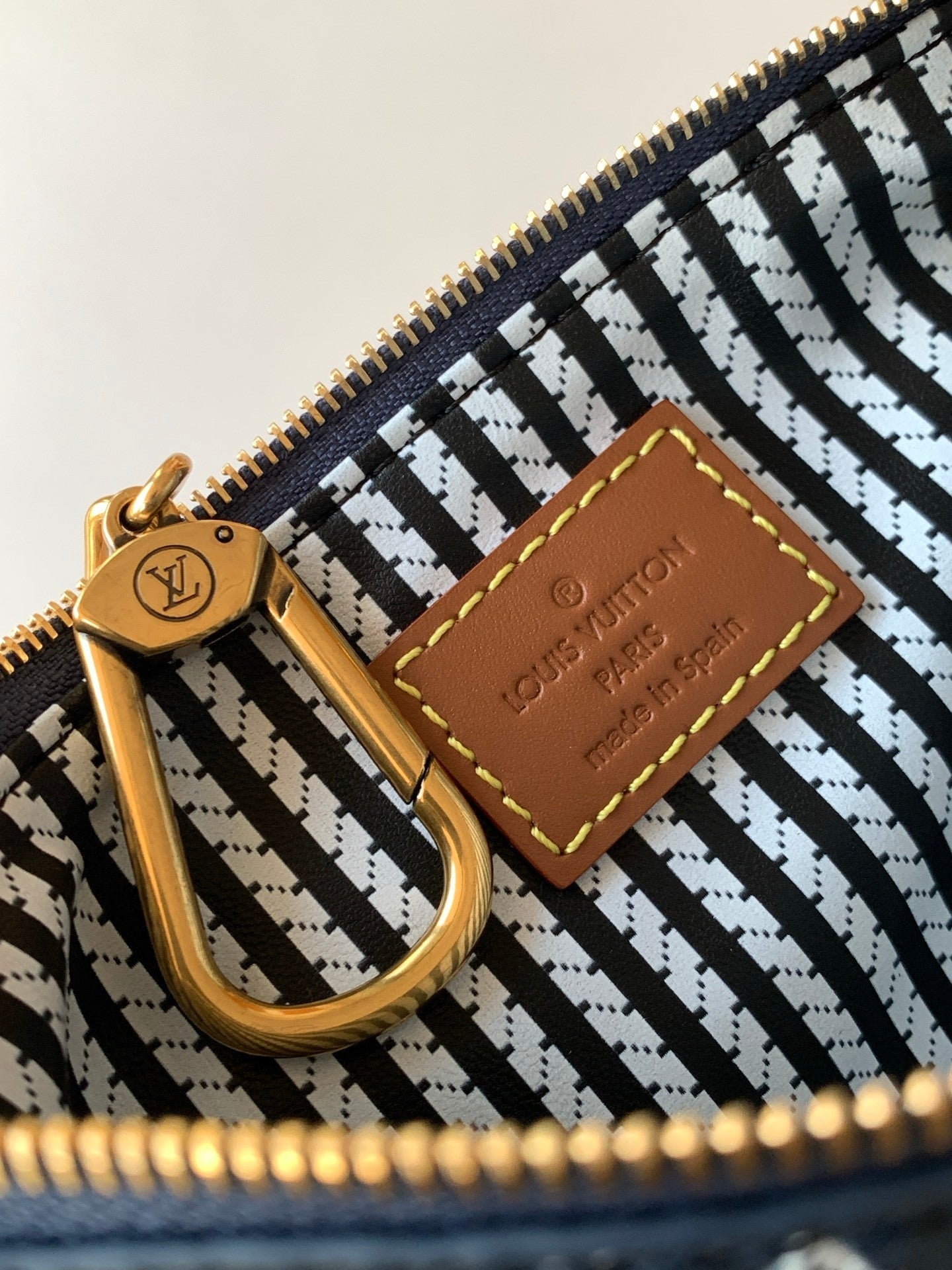 Designer handbag interior close-up with gold zipper pull and tan leather brand patch