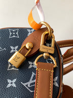 Designer handbag close-up of gold padlock charm and tan leather strap on navy monogram canvas