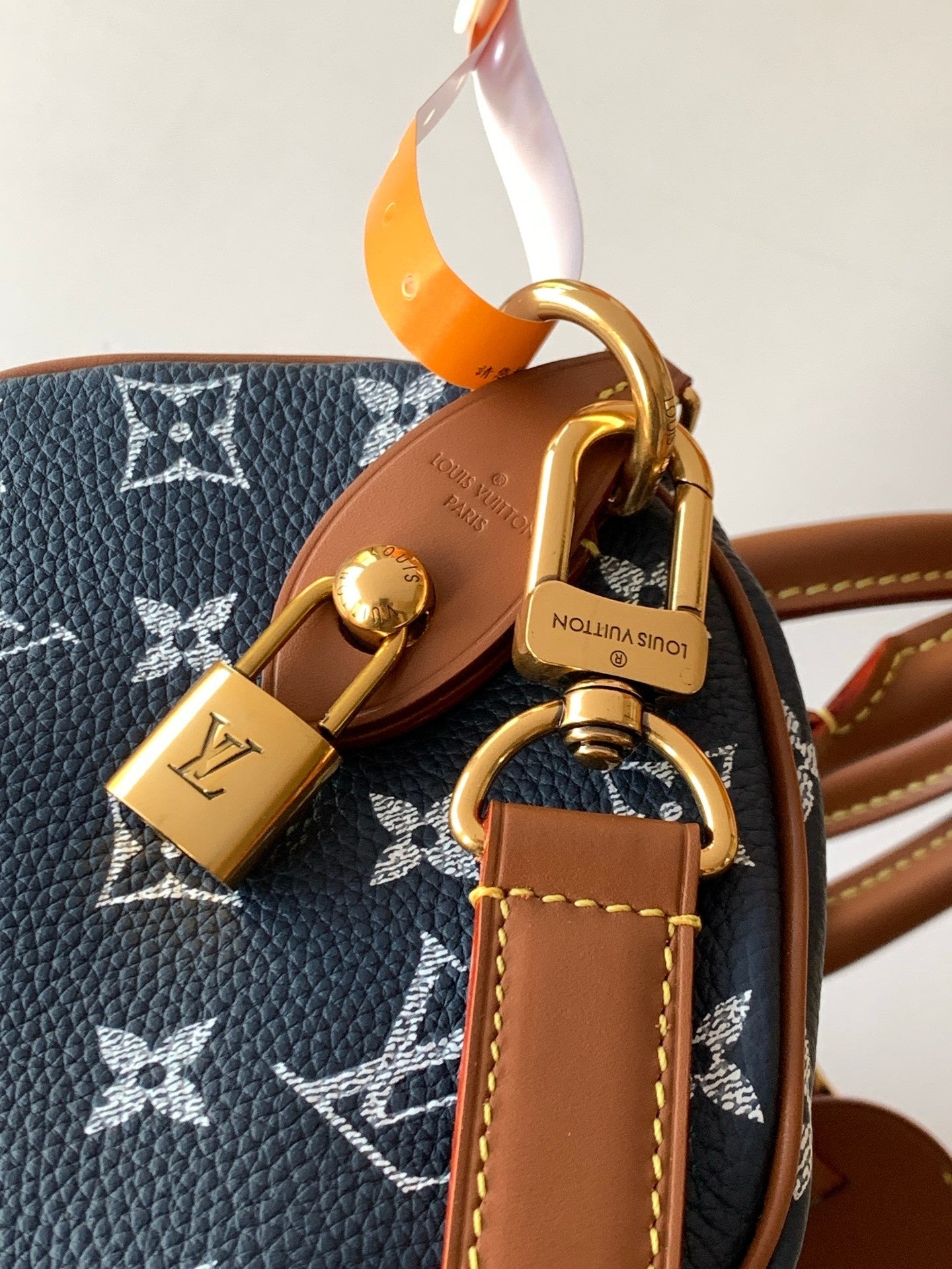 Designer handbag close-up of gold padlock charm and tan leather strap on navy monogram canvas