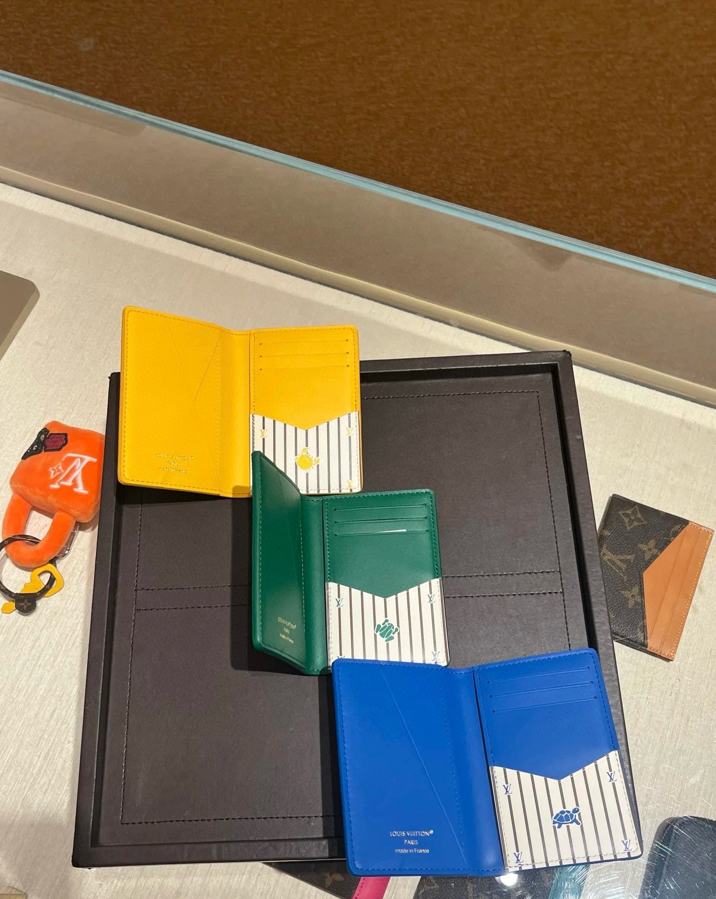 Small Louis Vuitton card holders in display, yellow, green, and blue with striped panels