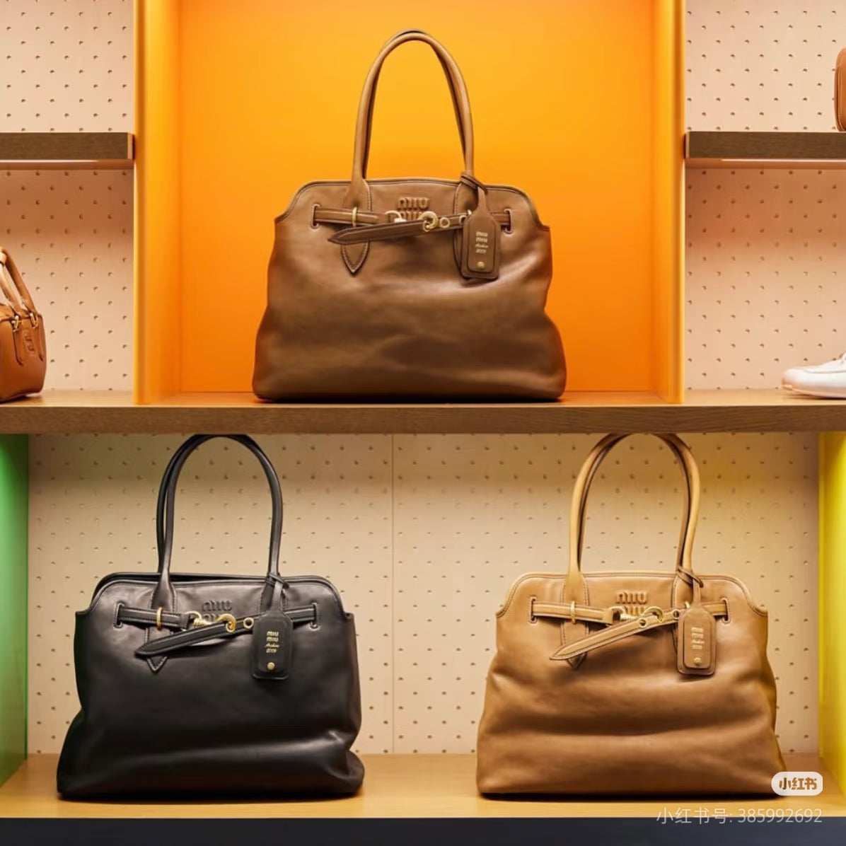 MiuMiu leather tote bags displayed on shelves in tan, dark brown, and black with gold hardware