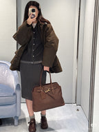 MiuMiu leather tote bag in dark brown with gold clasp and front logo tag, held at side
