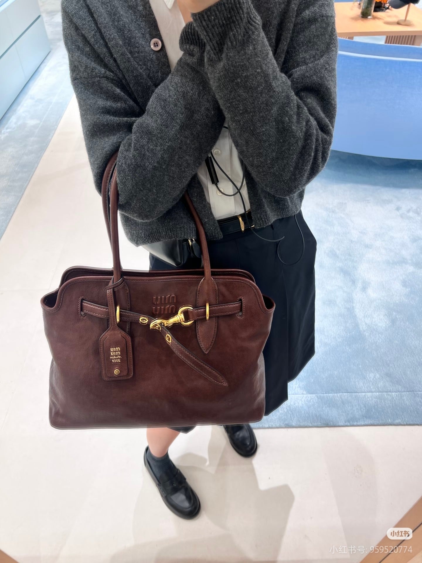 MiuMiu leather tote bag in dark brown with gold clasp and front logo tag, carried