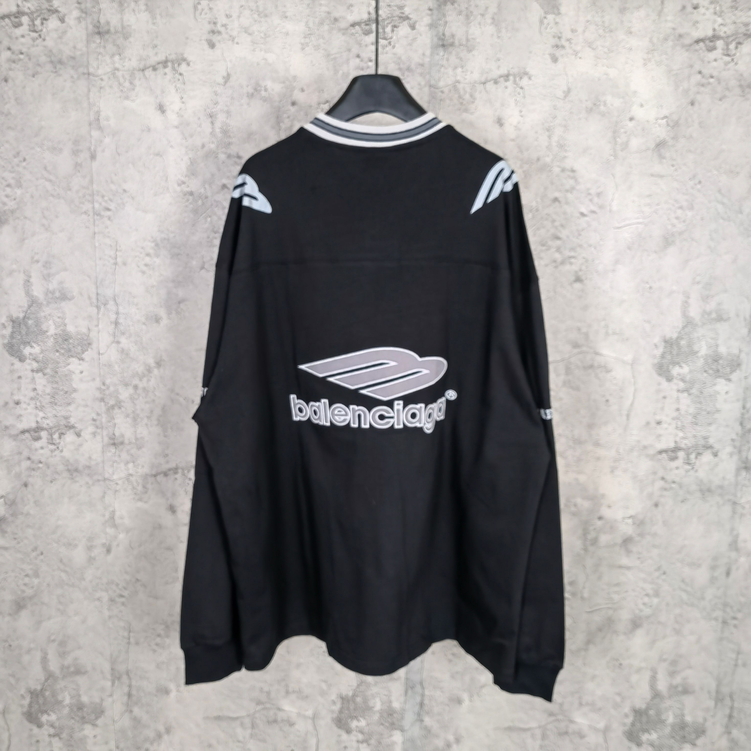 Black long-sleeve V-neck shirt with Balenciaga logo on back and sleeve stripe details.