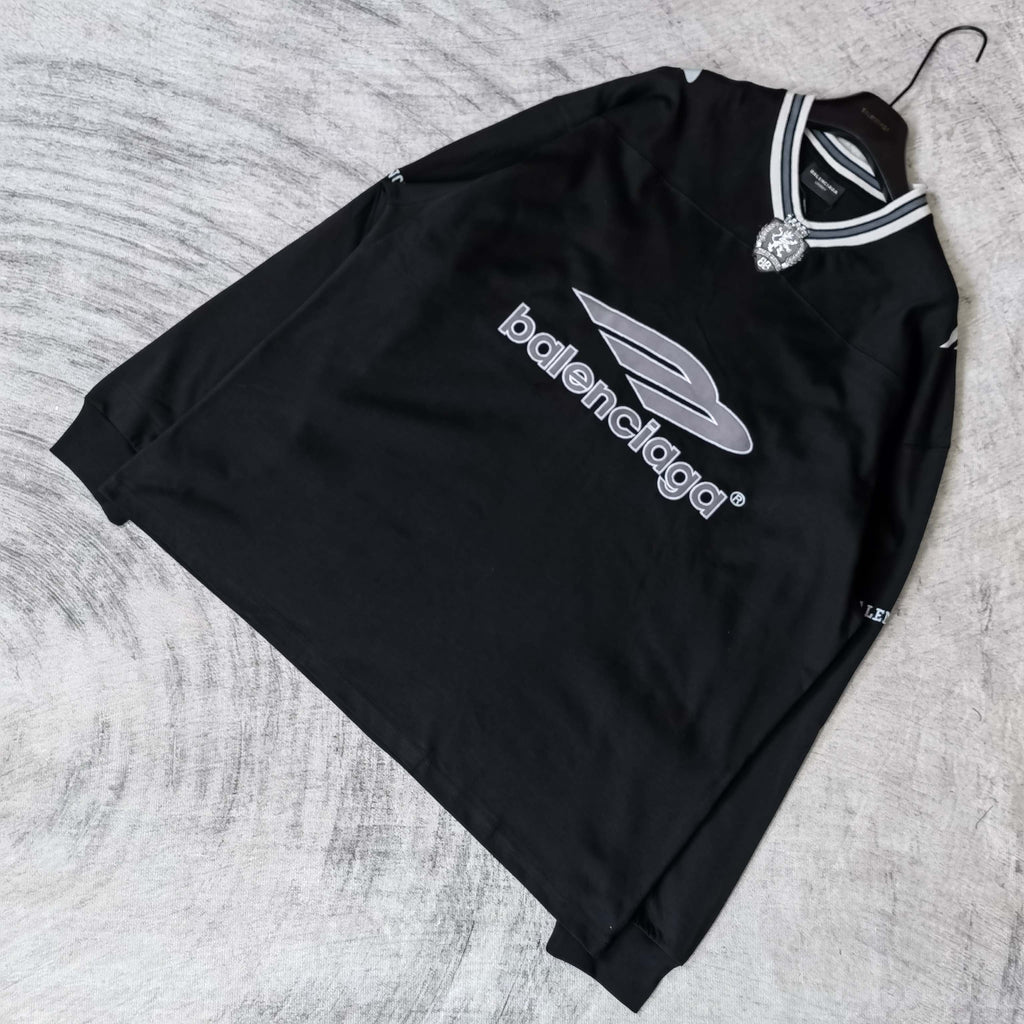 Black long-sleeve V-neck shirt laid flat with Balenciaga chest logo and striped collar.