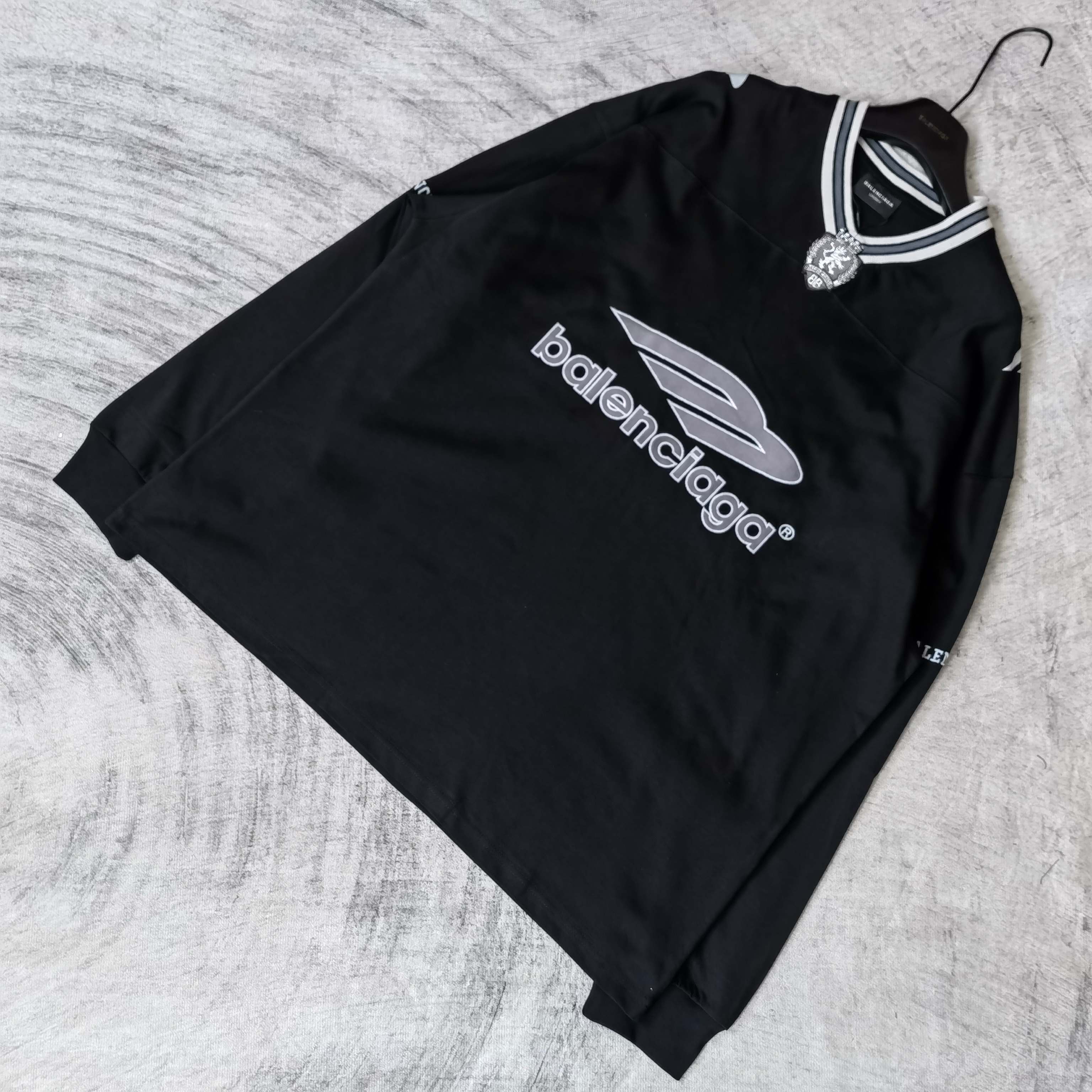Black long-sleeve V-neck shirt laid flat with Balenciaga chest logo and striped collar.