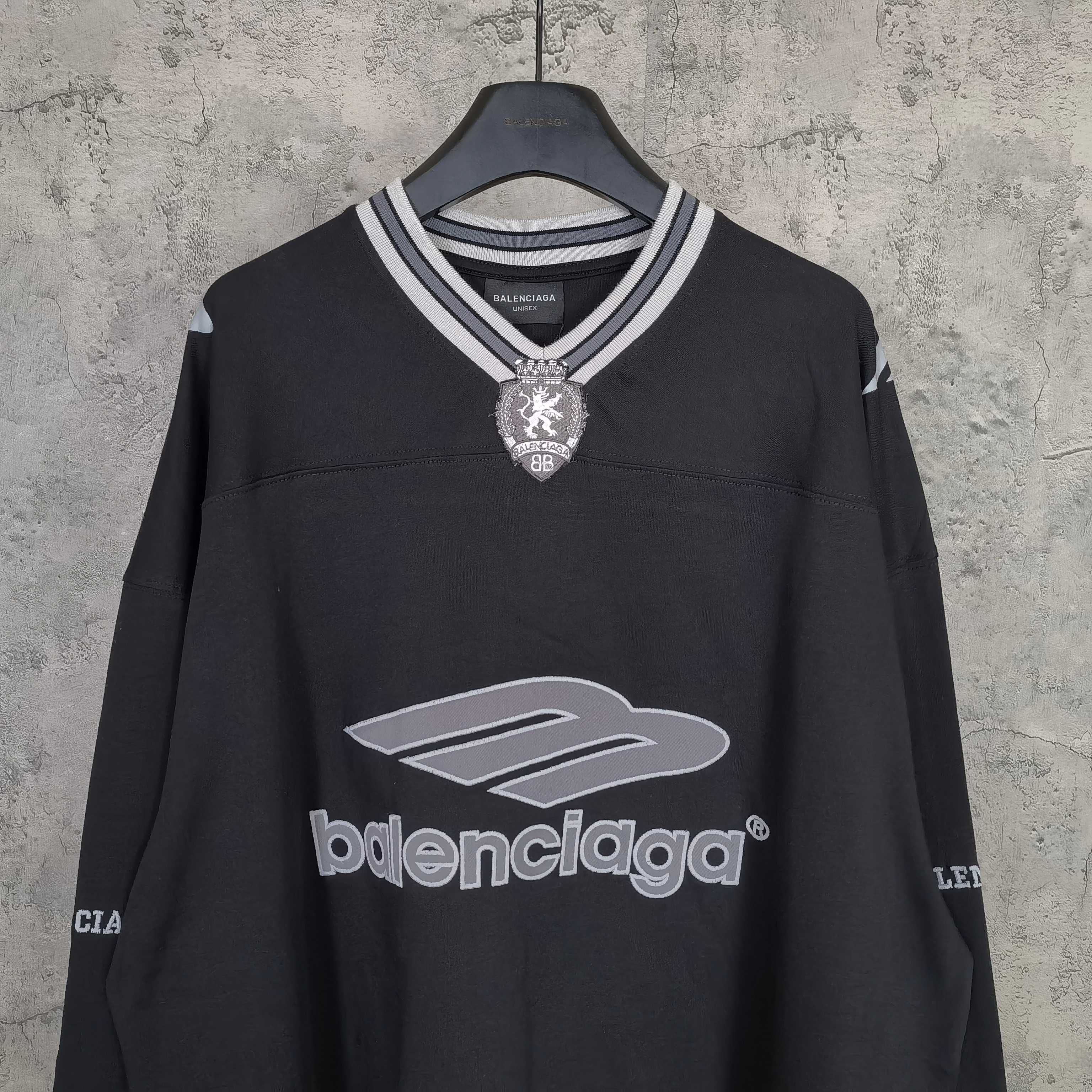 Black long-sleeve V-neck shirt with striped rib collar and crest pendant logo at chest.