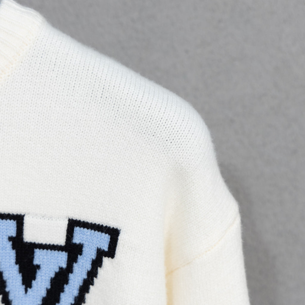 White knit sweater sleeve cuff with blue-and-black embroidered logo
