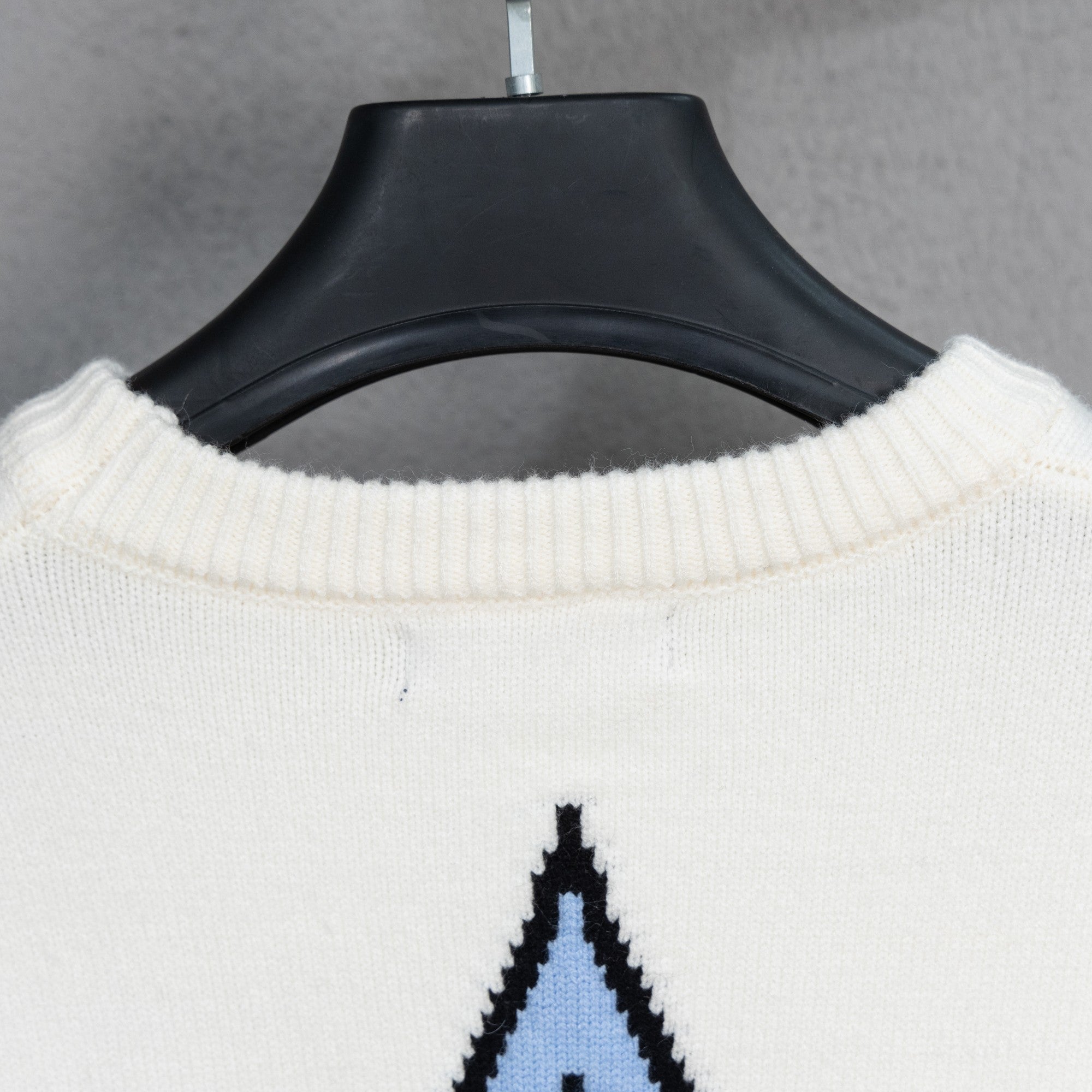 White ribbed crewneck sweater with black-and-blue logo graphic partially visible