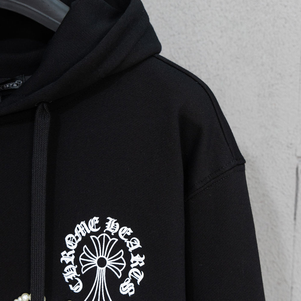 Black hoodie sleeve with pearl-studded cross-and-flower emblem on chest