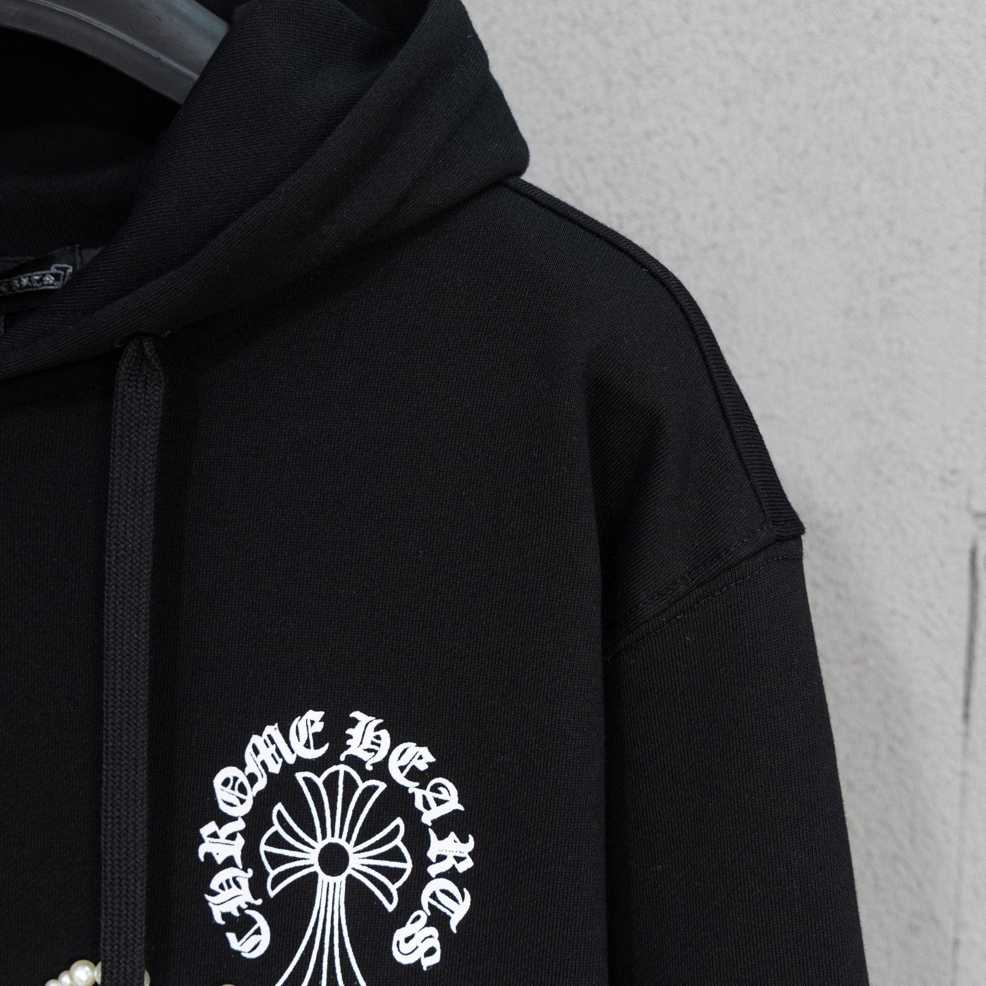 Black hoodie sleeve with pearl-studded cross-and-flower emblem on chest