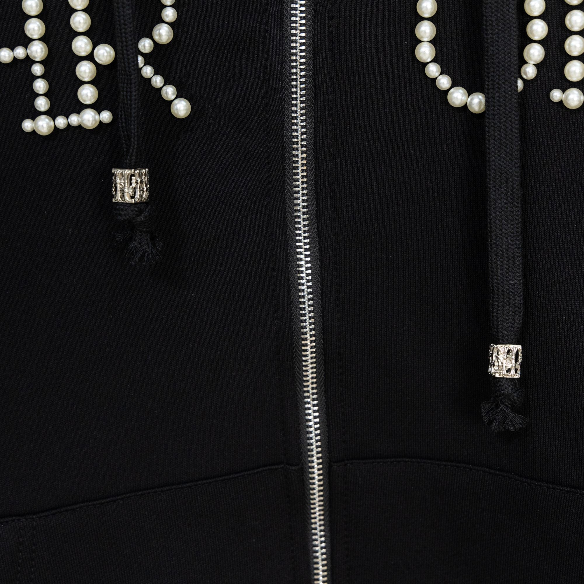 Black hoodie close-up of silver zipper and pearl beaded pocket detailing
