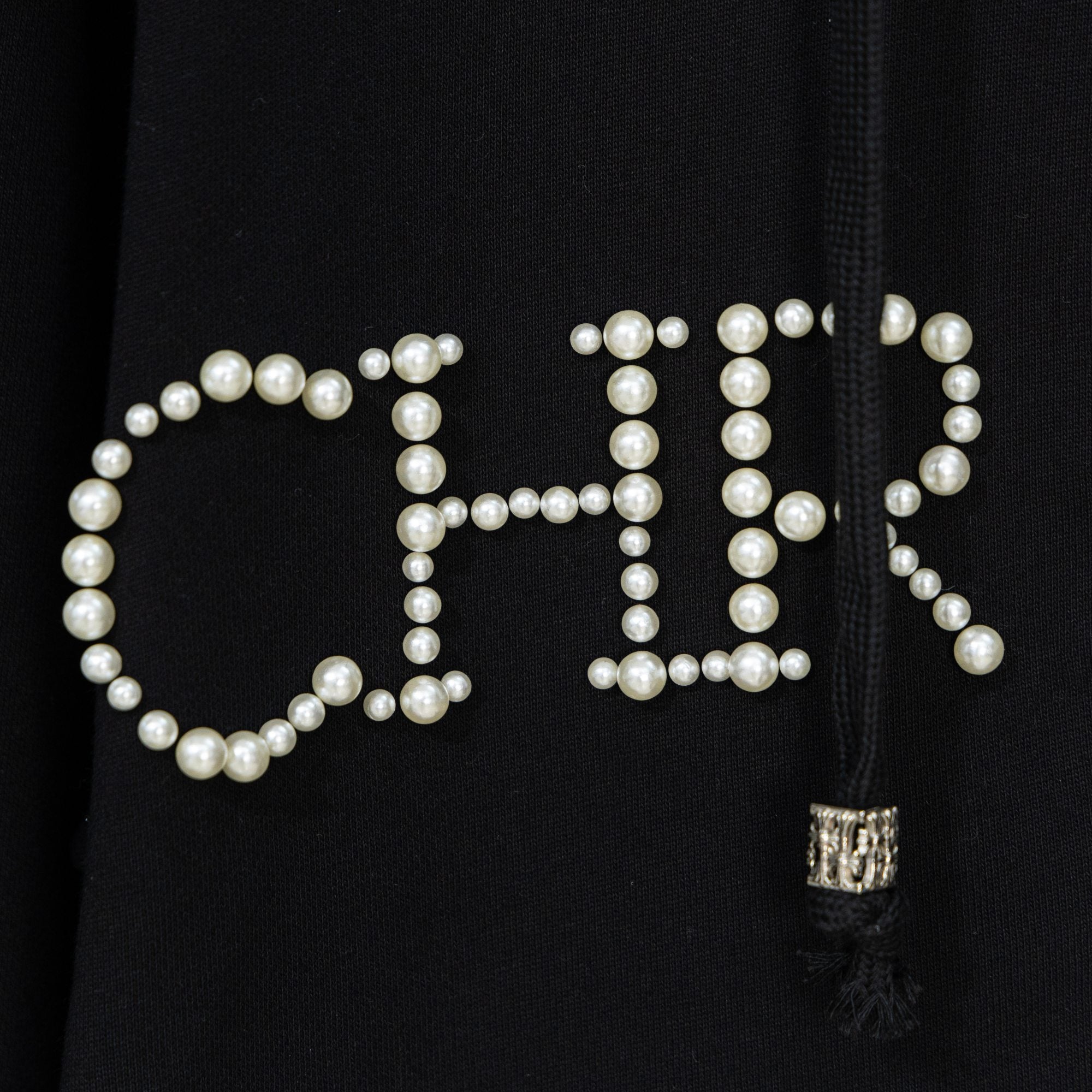 Black hoodie close-up of pearl beaded lettering with small zipper pull tassel
