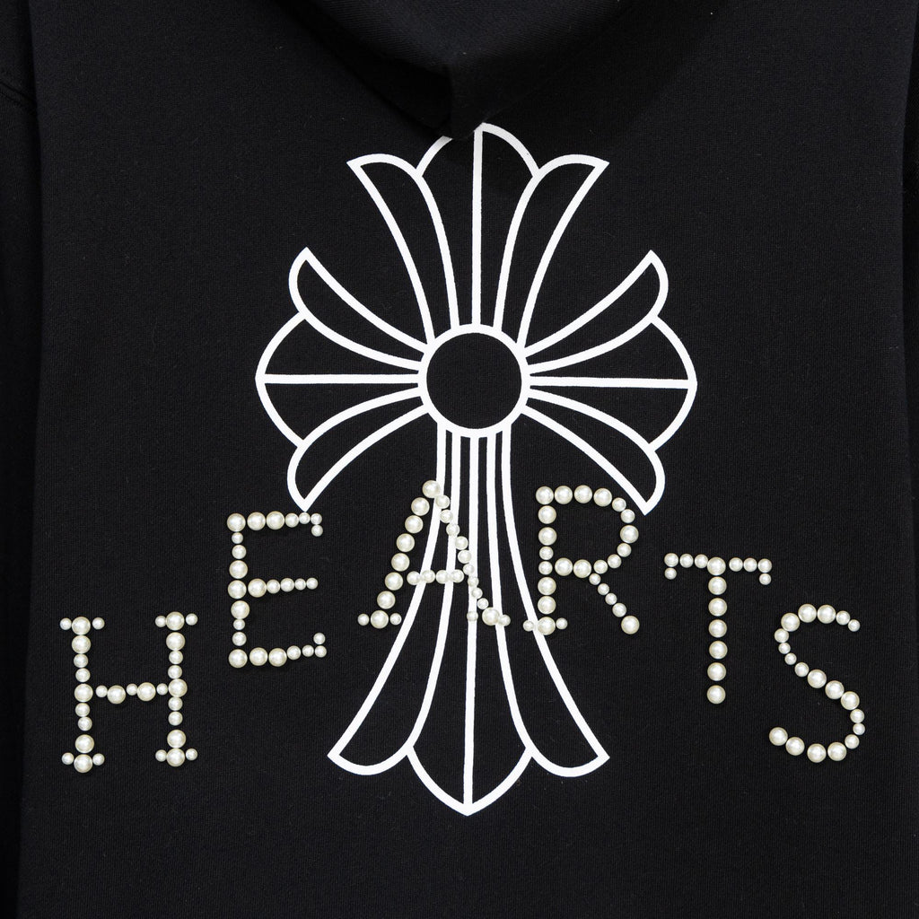 Black hoodie close-up of large pearl-studded crest and heart-shaped lettering