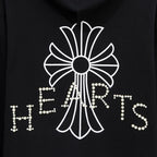 Black hoodie close-up of large pearl-studded crest and heart-shaped lettering
