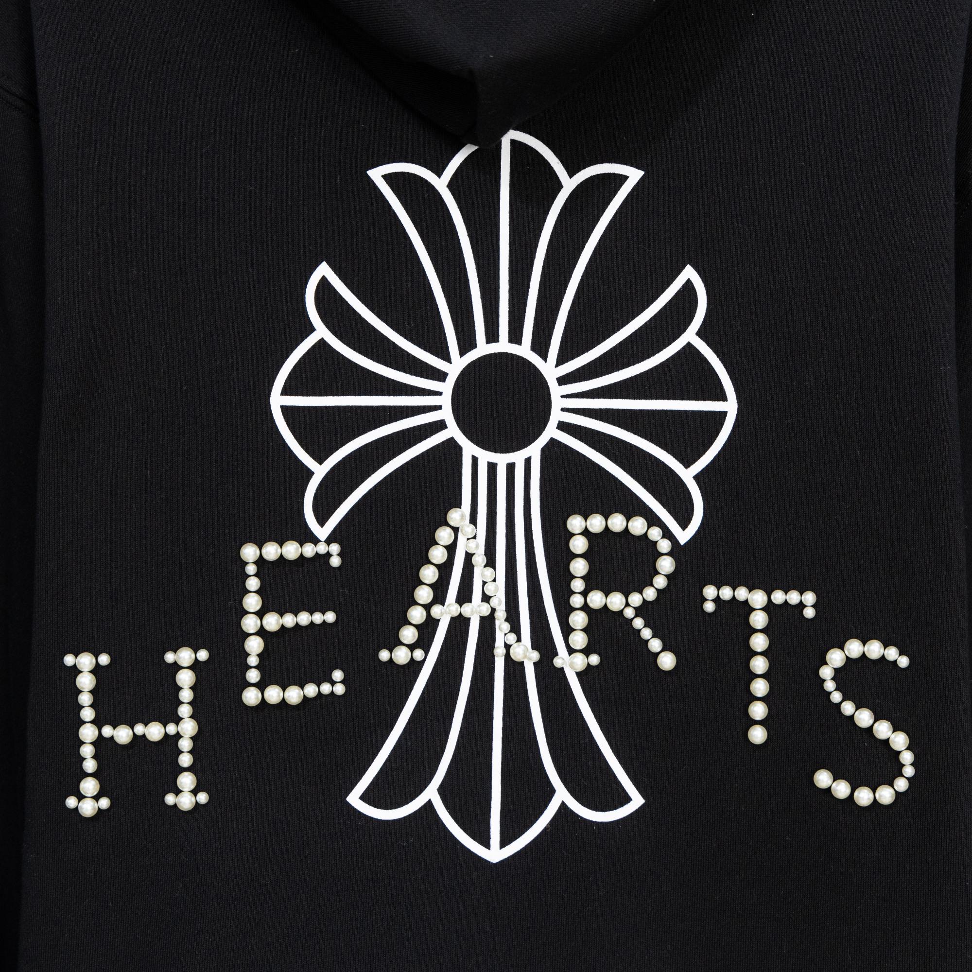 Black hoodie close-up of large pearl-studded crest and heart-shaped lettering
