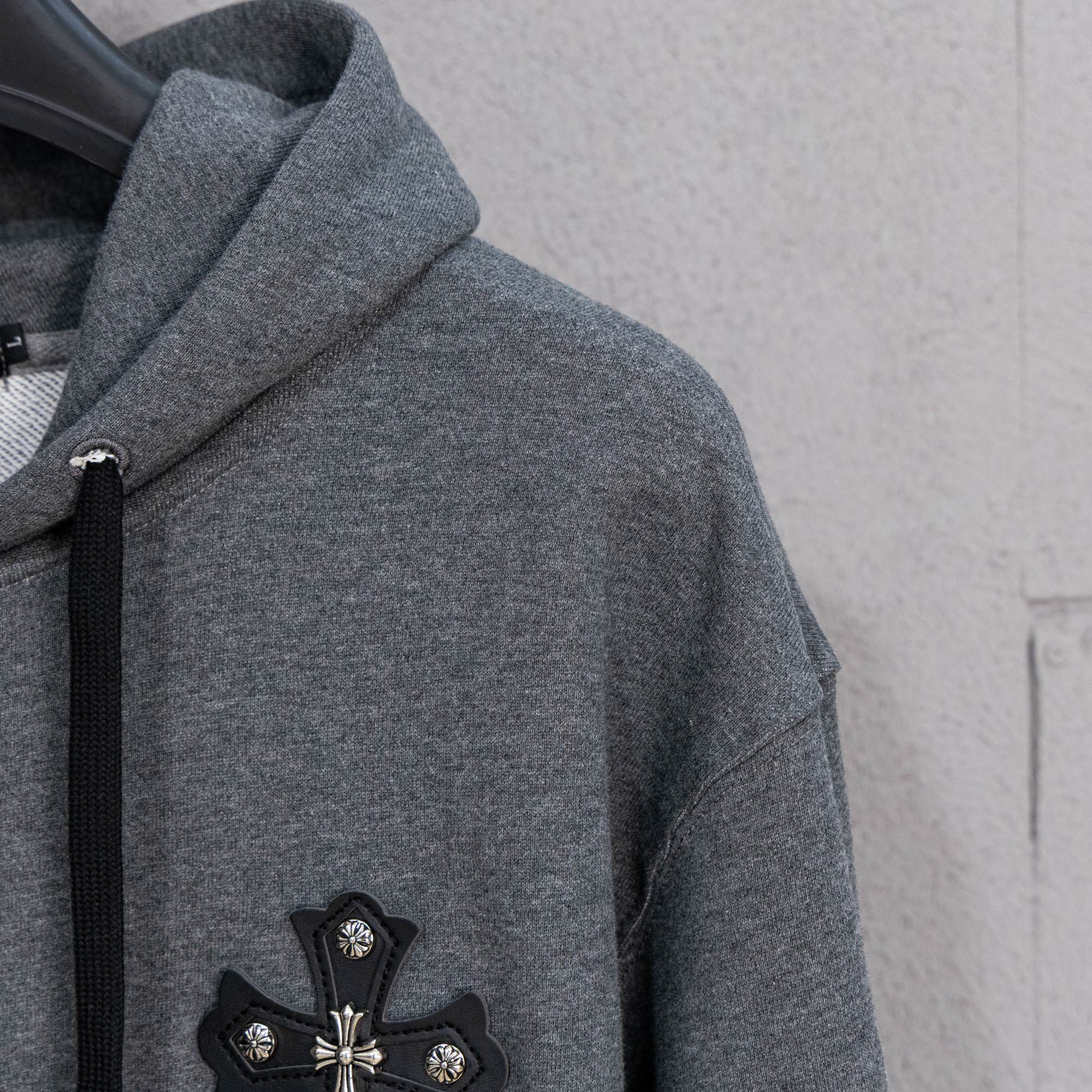 Grey hoodie side view with black cross appliqué on left chest
