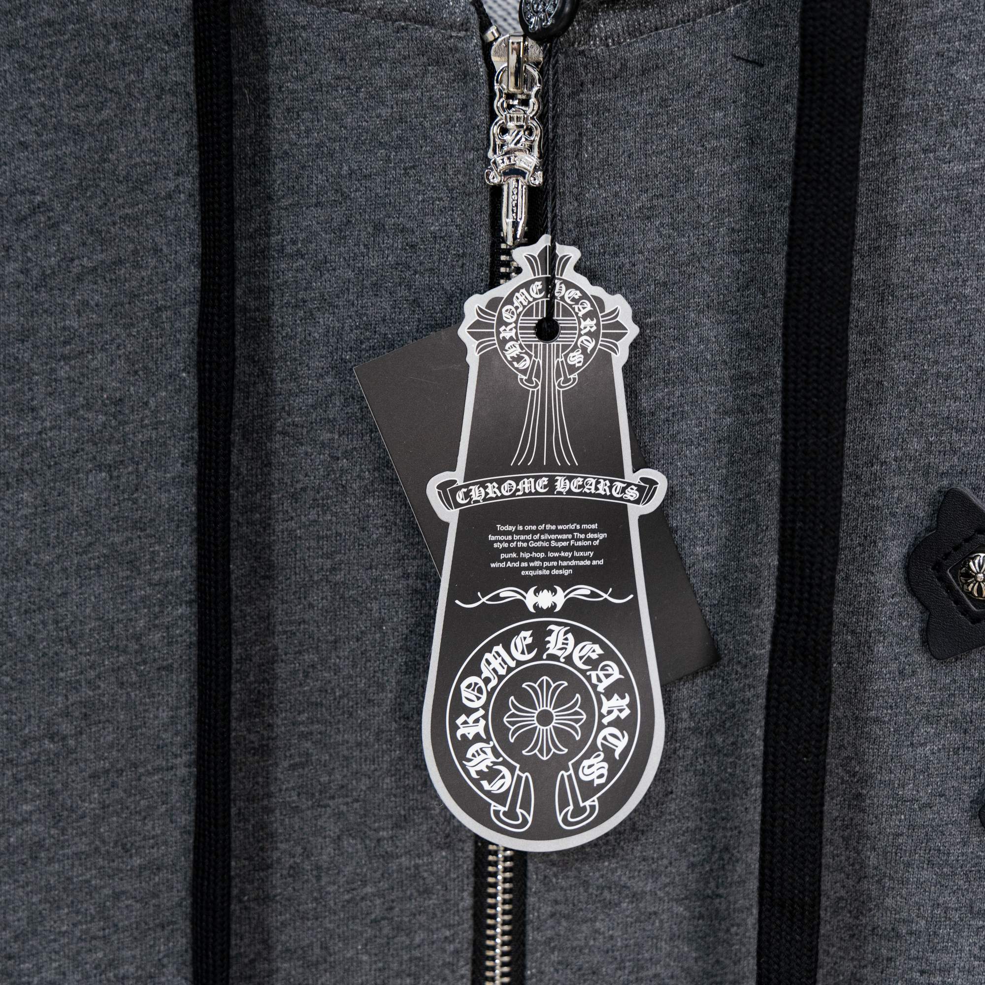 Grey hoodie front close-up showing silver zipper pull and charm tag