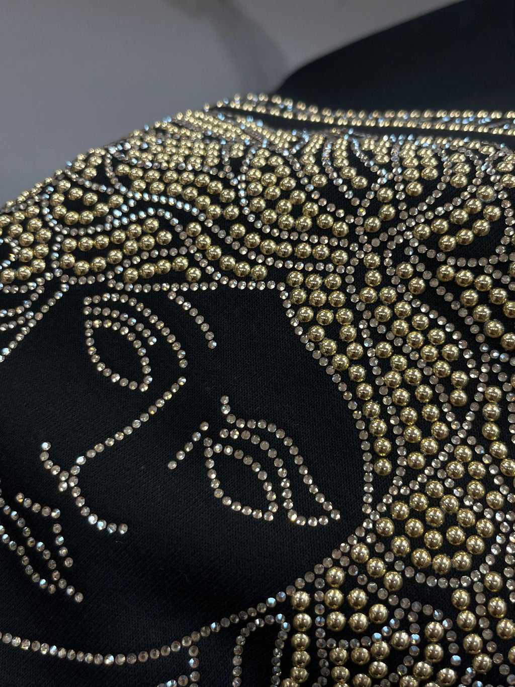 Black crewneck sweatshirt front detail with gold rhinestone face motif