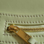 Gold-tone zipper pull with engraved accent on light yellow-green leather