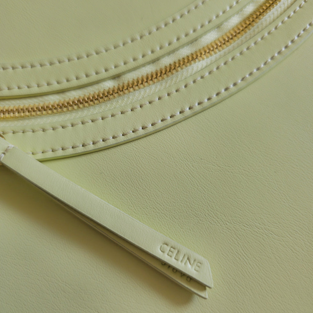 Close-up of gold zipper and stitched leather edge on light yellow-green bag