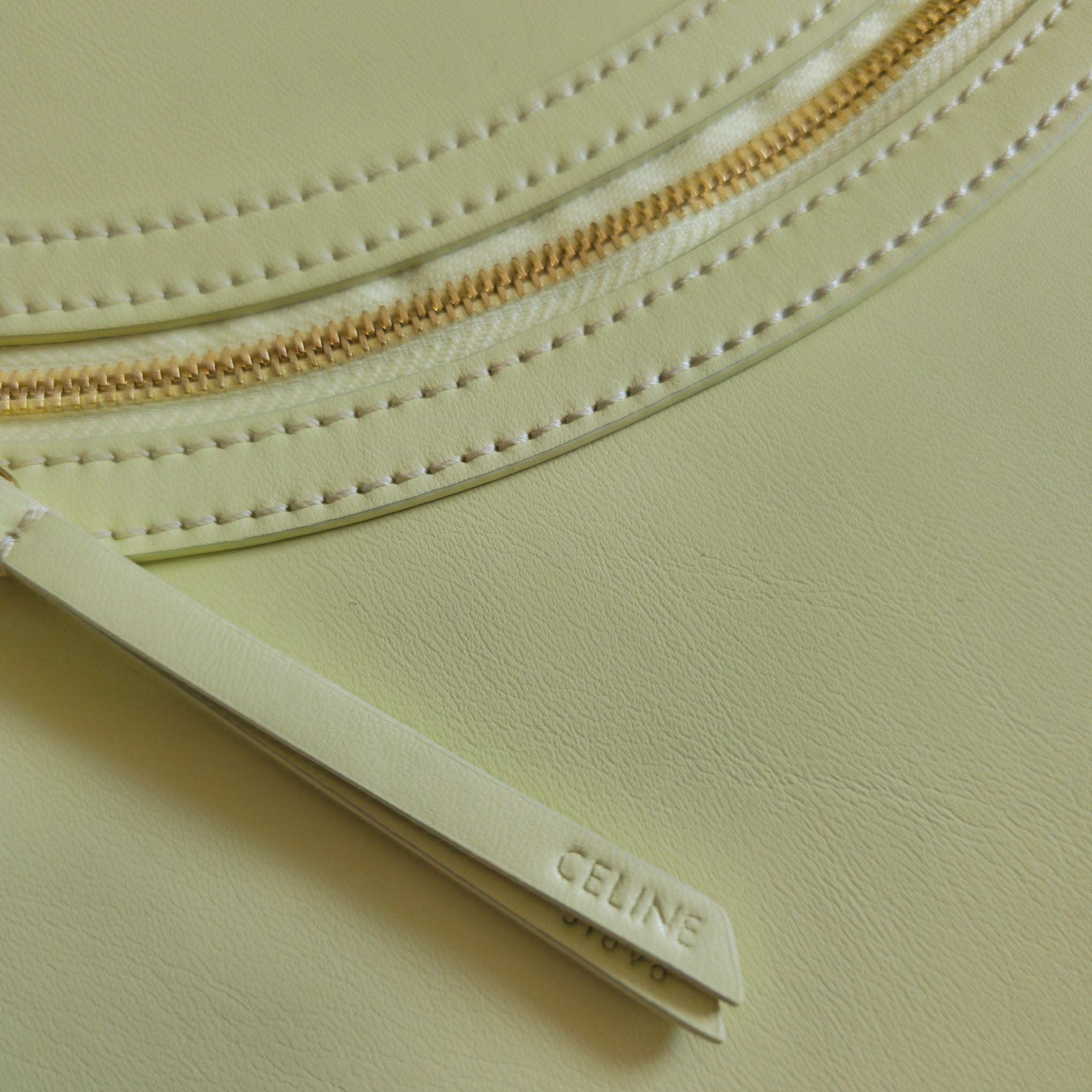 Close-up of gold zipper and stitched leather edge on light yellow-green bag