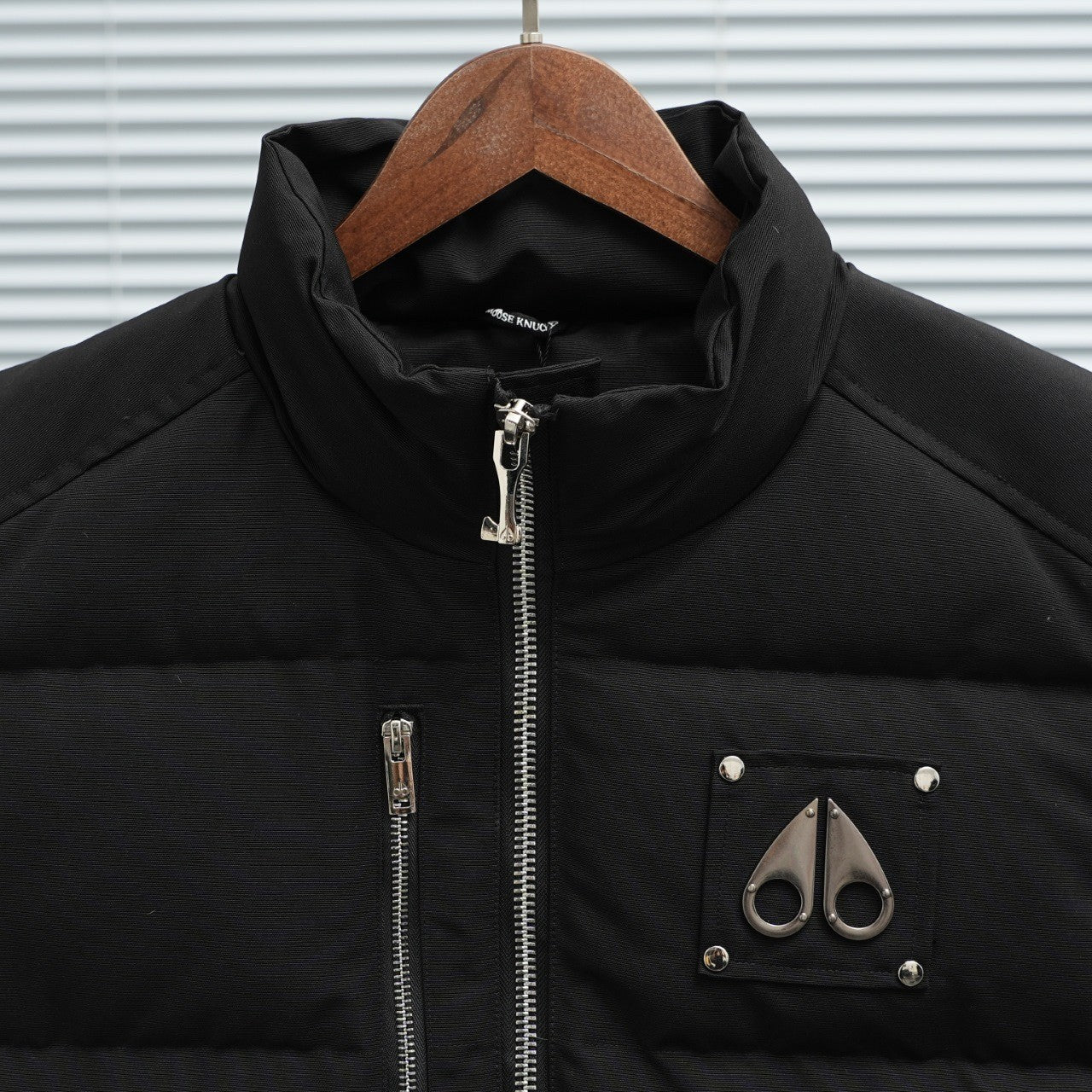 Black sleeveless puffer vest with stand collar, central zipper, and chest logo