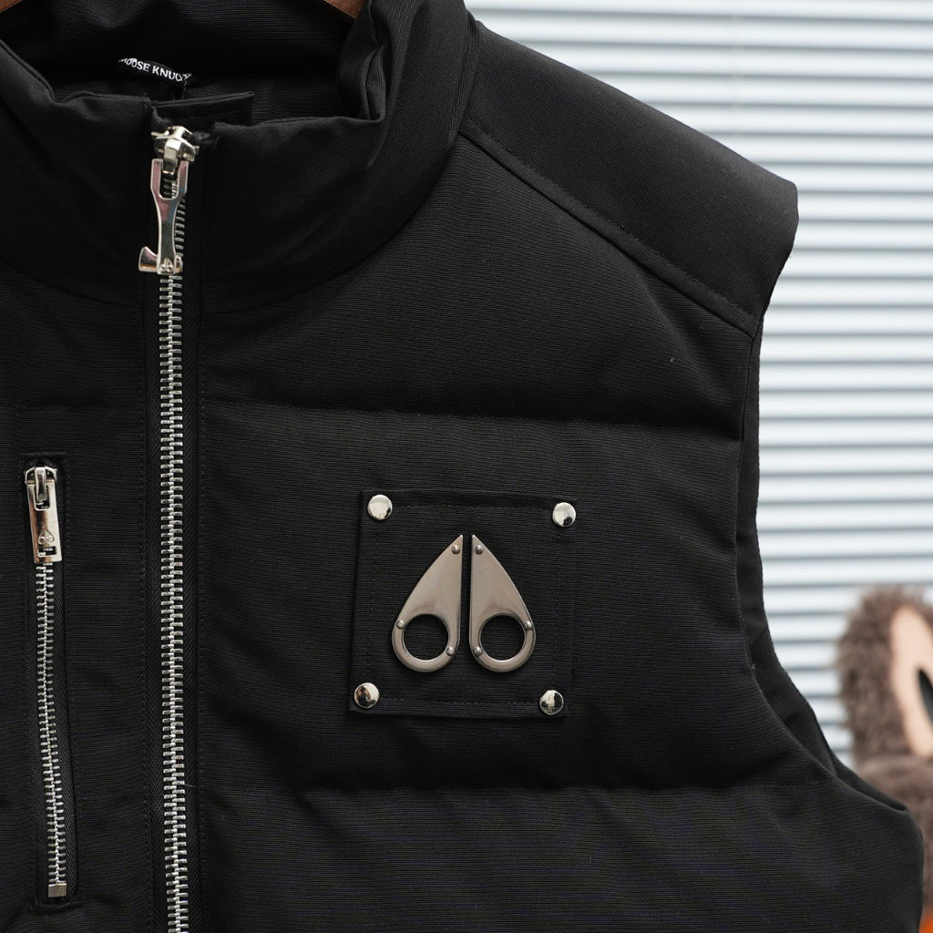 Black sleeveless puffer vest with chest logo patch and snap-front pockets