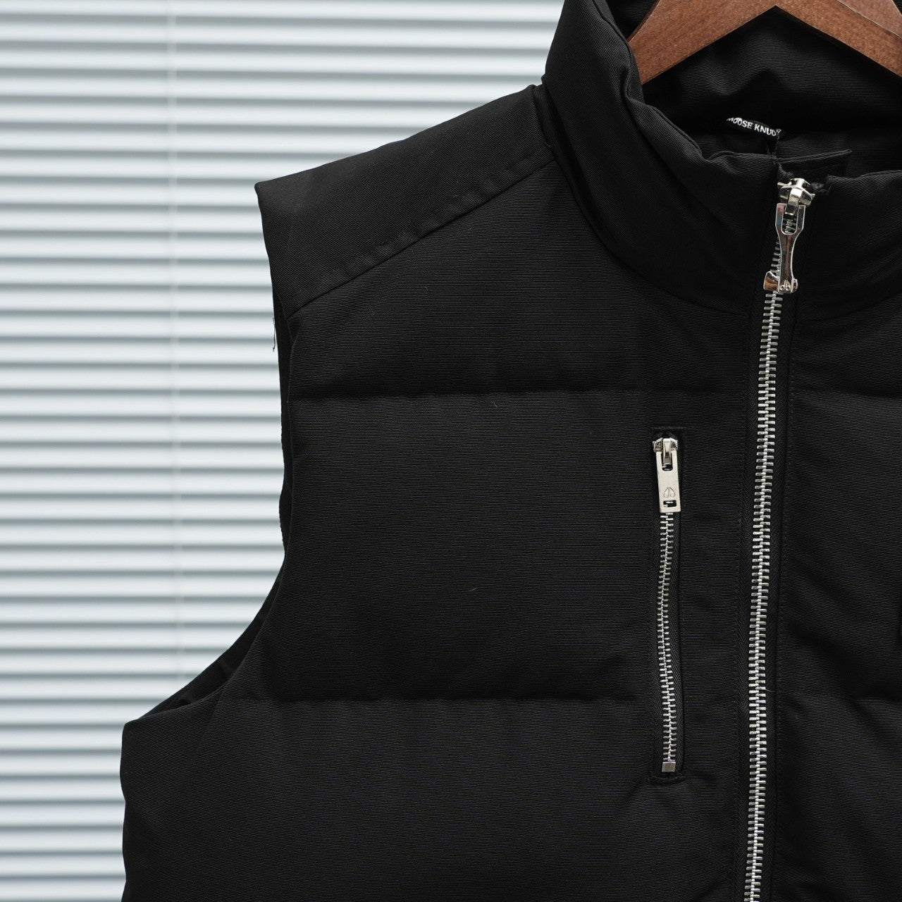 Black sleeveless puffer vest panel with central zipper and silver zip pull