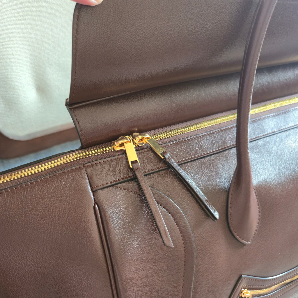 Brown leather tote bag close-up of gold zipper pull and front strap detail