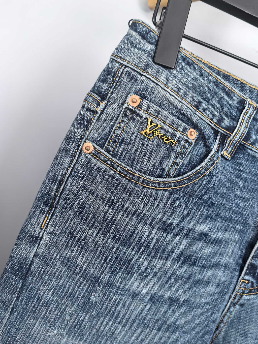 Blue denim pants front close-up with branded pocket patch and copper buttons