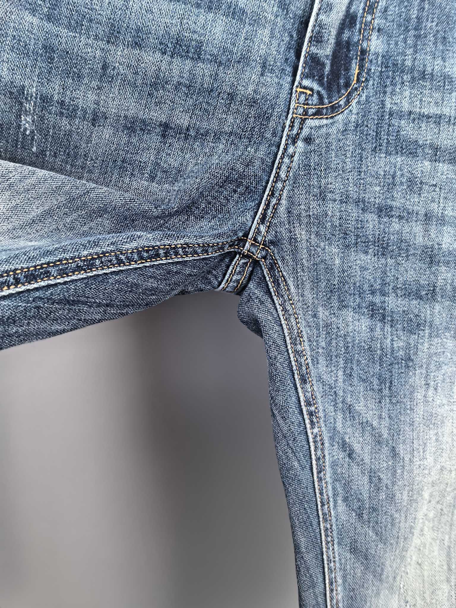 Close-up of blue denim side seam and leg with stitched cuff and pocket edge