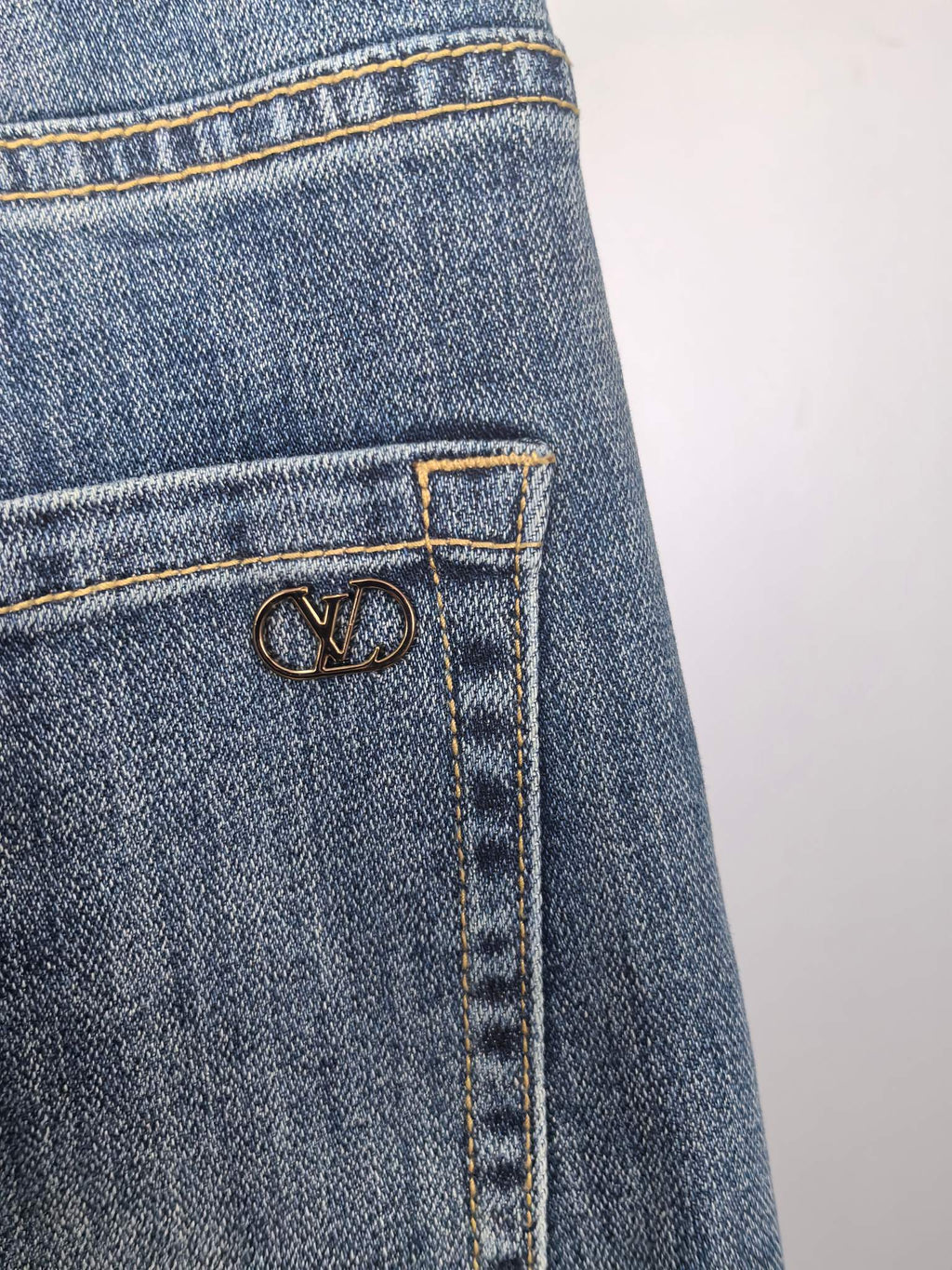 Close-up of blue denim pocket with LV-style metal emblem on stitch panel