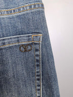 Close-up of blue denim pocket with LV-style metal emblem on stitch panel