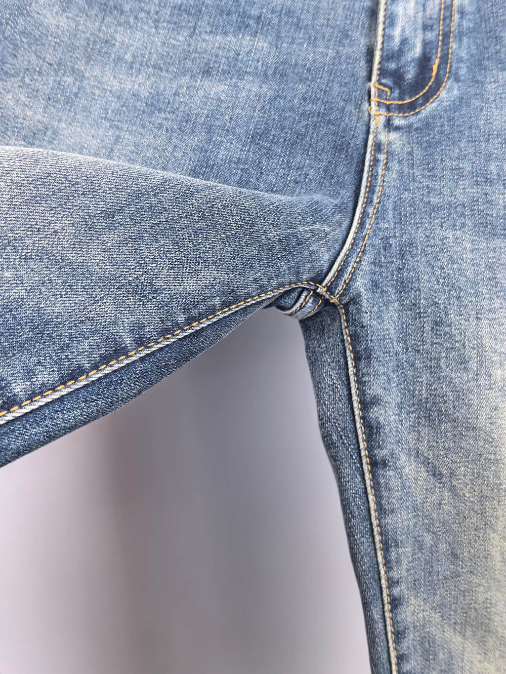 Blue denim pants side with belt loop and seam-stitch detail near knee