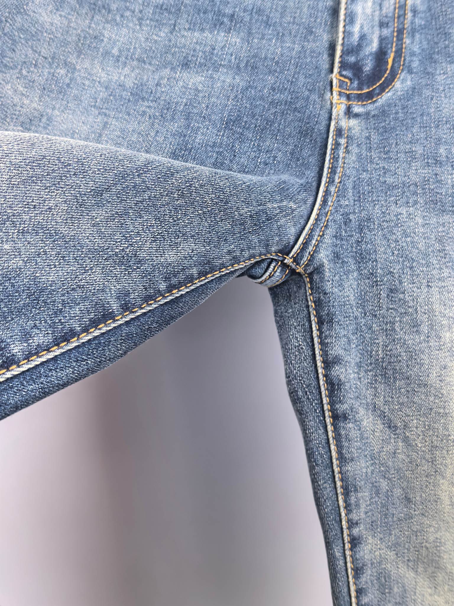 Blue denim pants side with belt loop and seam-stitch detail near knee