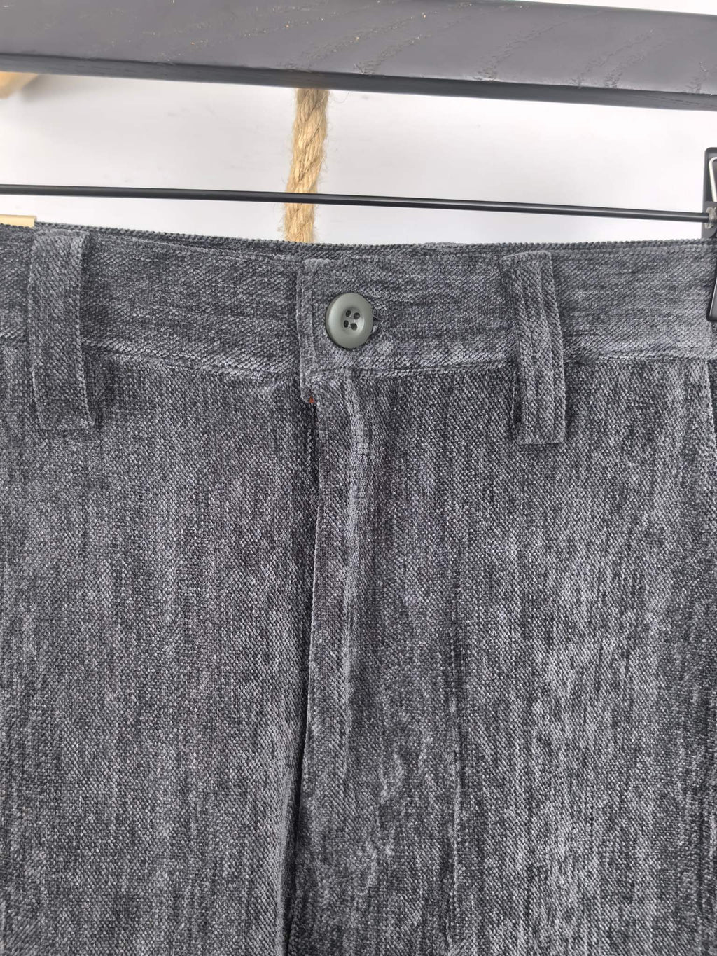 Charcoal trouser waistband with button closure, belt loops, and front fly detail.