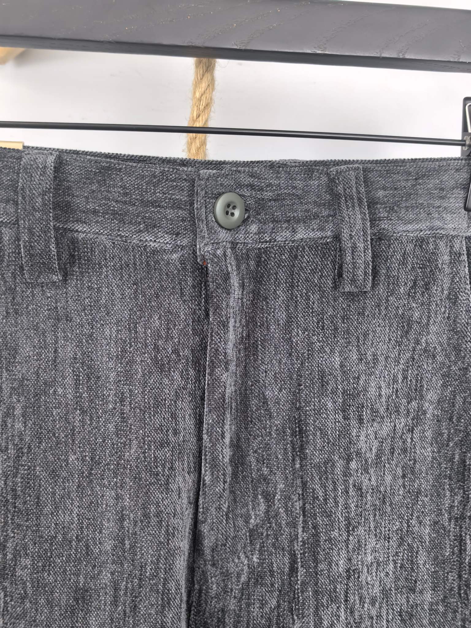 Charcoal trouser waistband with button closure, belt loops, and front fly detail.