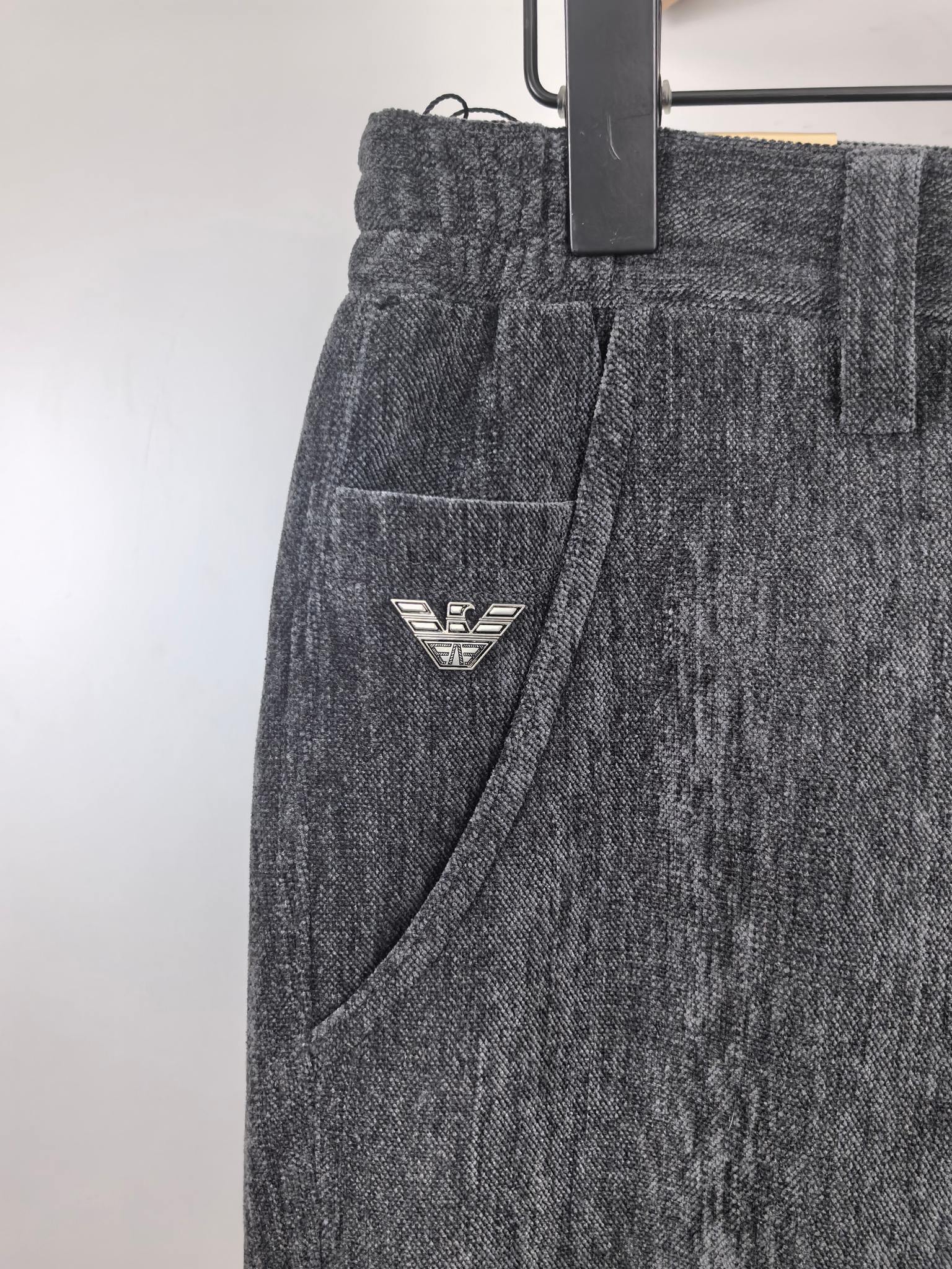 Charcoal trousers with side pocket and small triangular logo patch near the thigh.