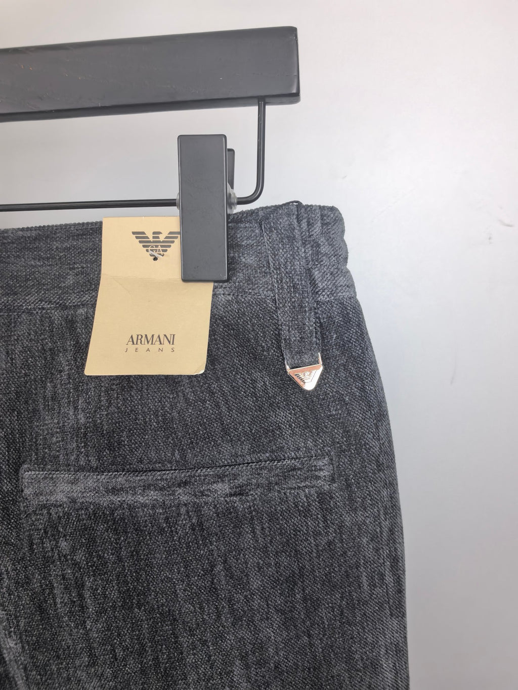 Charcoal trousers with belt loops and triangular logo patch near the front pocket area.