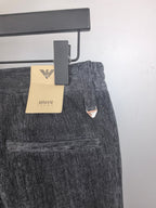 Charcoal trousers with belt loops and triangular logo patch near the front pocket area.