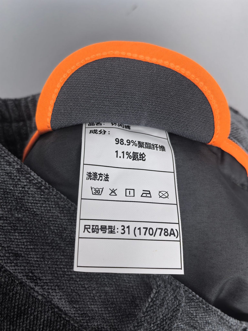 Orange-trimmed interior label with fabric and care info for dark charcoal trousers.