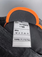 Orange-trimmed interior label with fabric and care info for dark charcoal trousers.