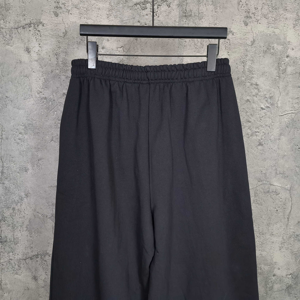 Balenciaga black pants with elastic waistband, draped fabric, front view on hanger